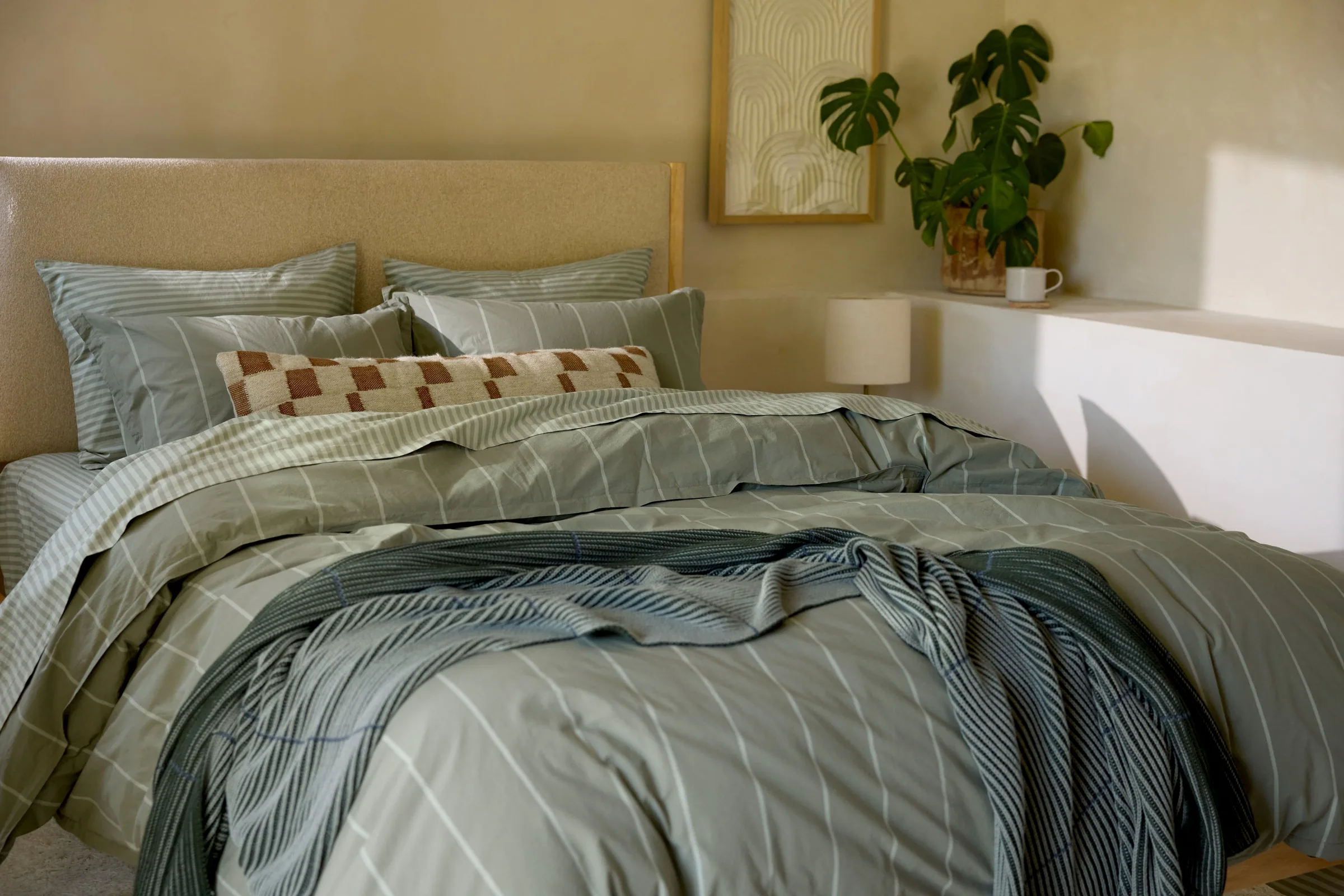 A Parachute bed made up in sage striped bedding with layered pillows in a sunlit room.